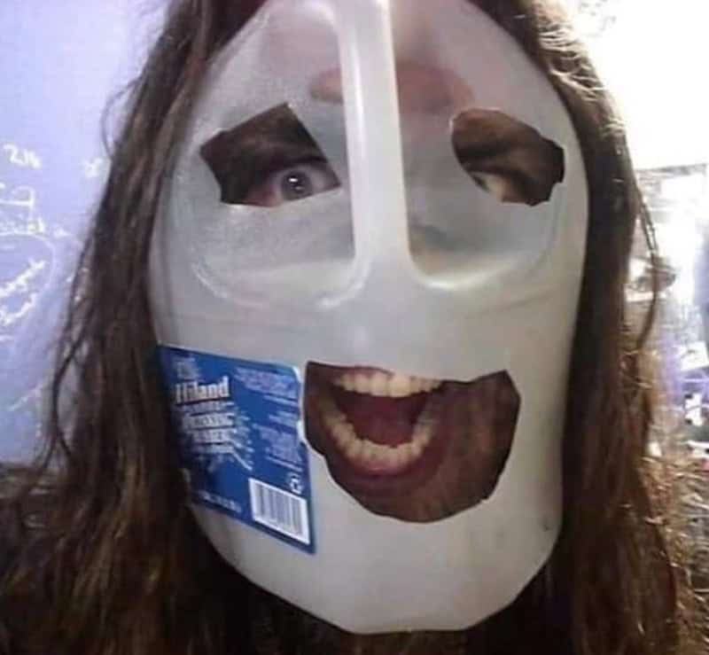 Person wearing a white plastic jug mask with cutouts for eyes and mouth, wide smile visible.