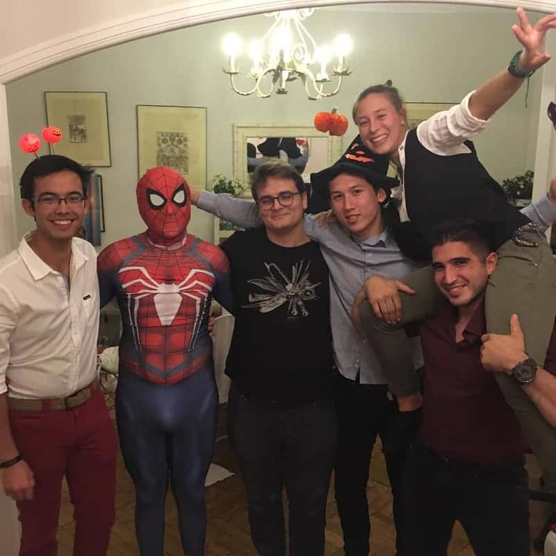 Group of friends at Halloween party, one dressed as Spider-Man with red spider emblem on blue suit,.