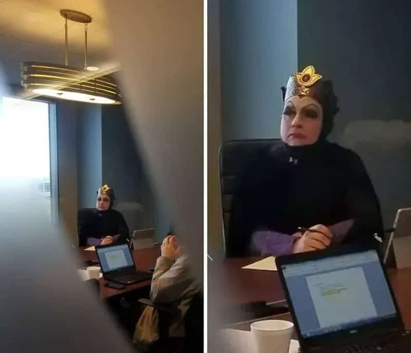 Person wearing a crown-like headpiece seated at a conference table, dark clothing, in a meeting room.