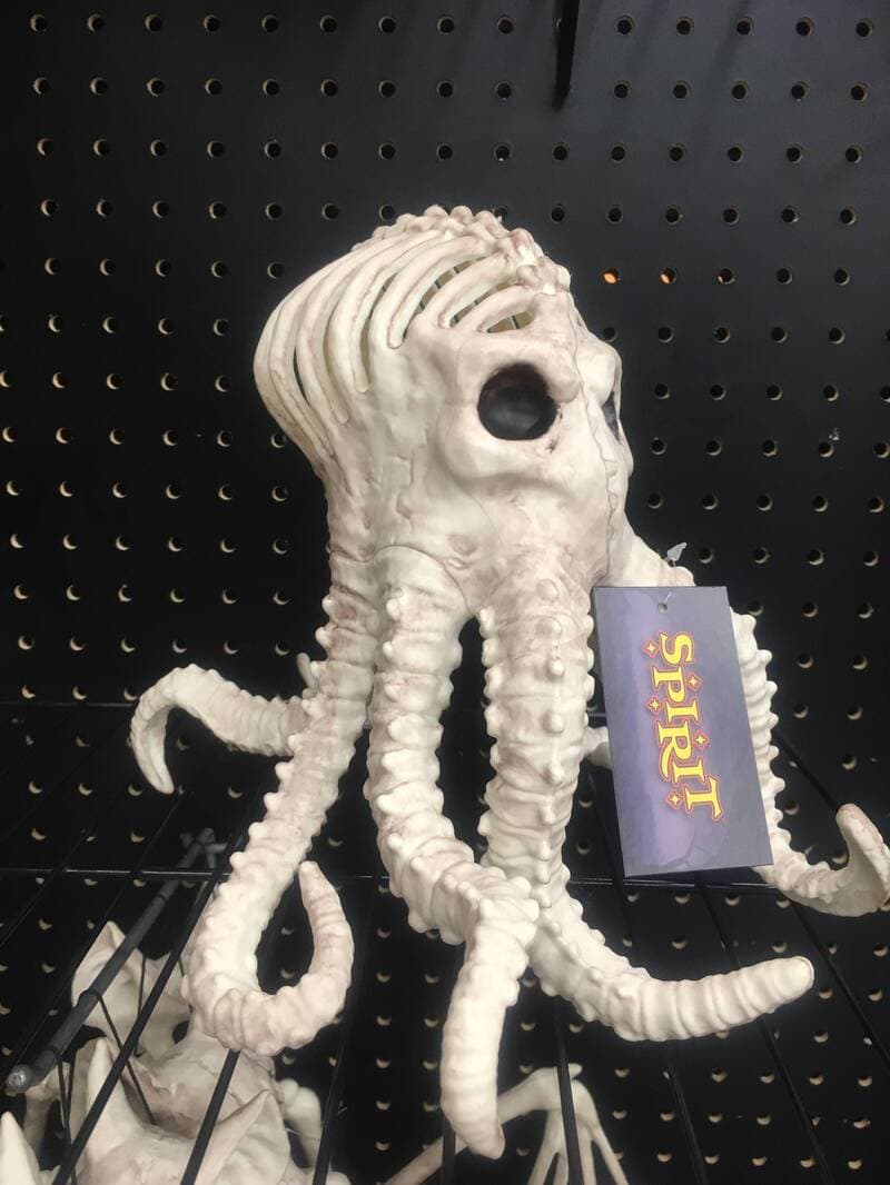 Astronaut-like squid creature prop with multiple tentacles on a black pegboard background; tag reads.