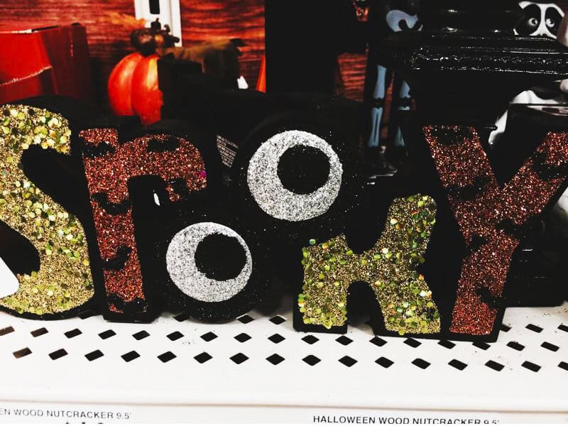Glittery Halloween decor letters spelling 'SPOOKY' on a shelf with a small pumpkin in background.