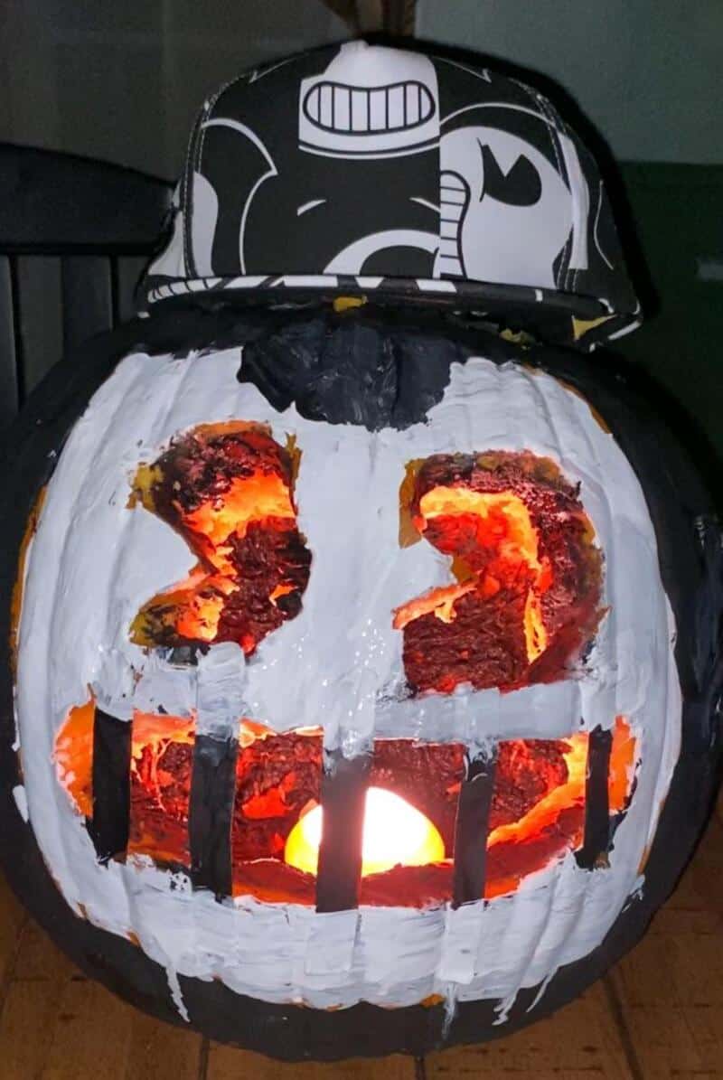 A carved jack-o'-lantern with a wide, glowing grin and rectangular teeth, wearing a black-and-white,.