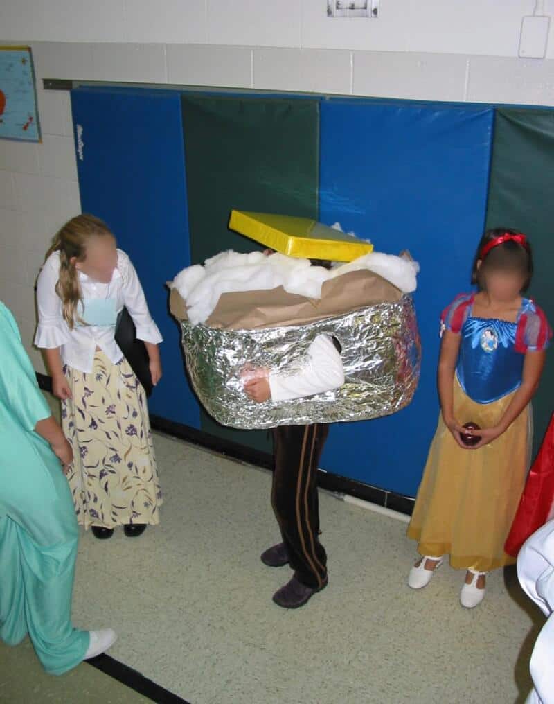Kids in costumes around a person wearing a craft-made box as a prop, in a school hallway.