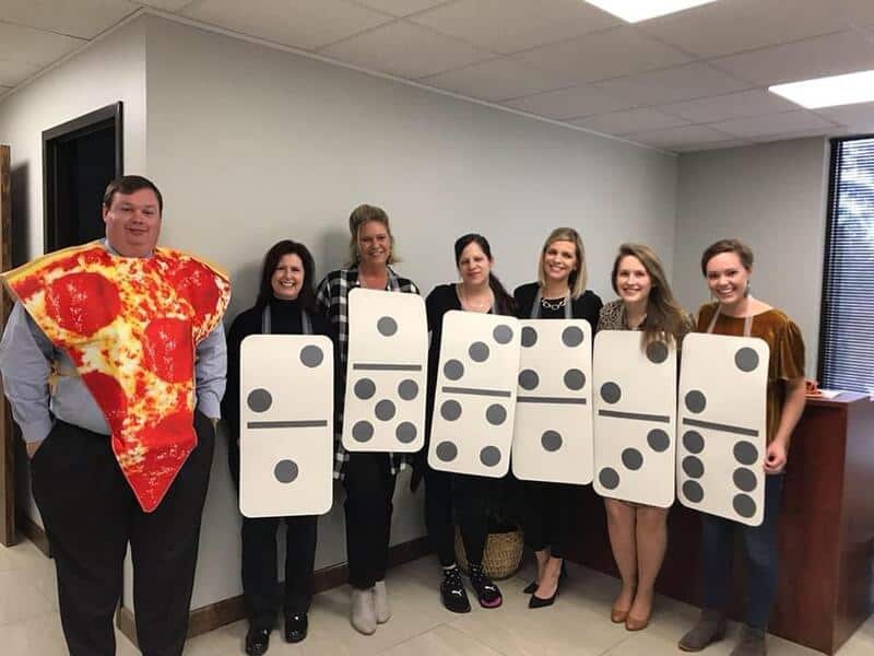 Group of coworkers wearing oversized domino costumes posing in an office hallway.