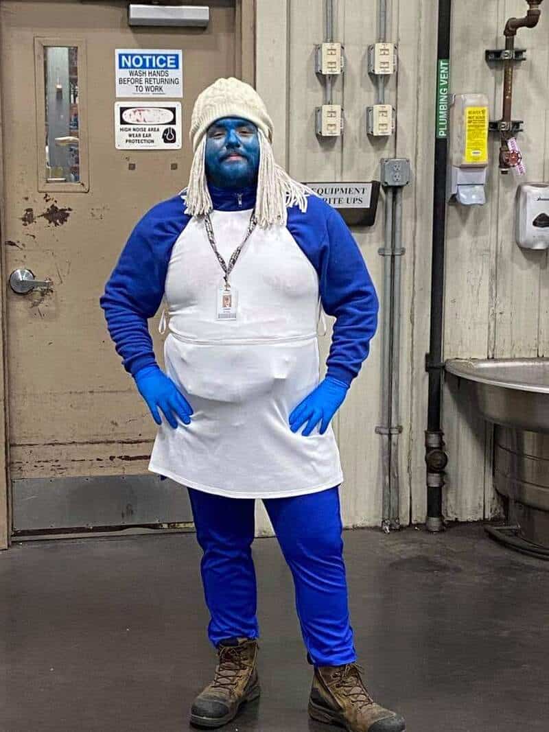 Person dressed as a Smurf with blue face paint, white hair, and a white apron.