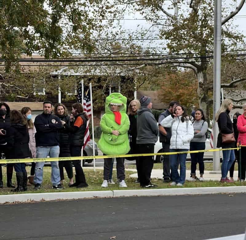 People in line with a person in a T-Rex costume at a Halloween event.