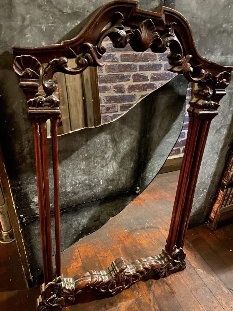 Broken ornate wooden mirror with cracked glass in a vintage setting.
