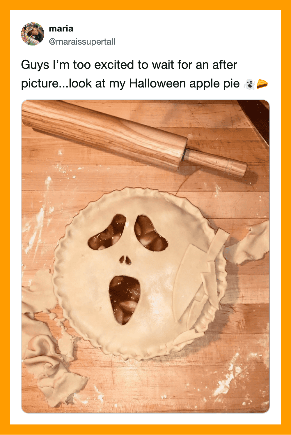 Halloween apple pie with a skull face design and rolling pin on wooden surface.