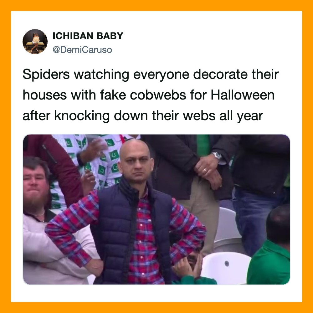 Man with hands on hips watching Halloween decorations, surrounded by people.