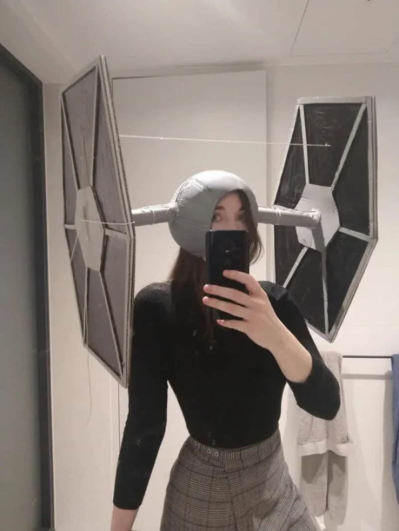 Person wearing a gray TIE fighter helmet from Star Wars, taking a mirror selfie in a bathroom.