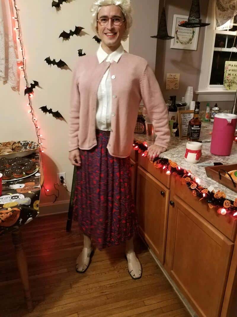 Person in pink cardigan, white blouse, and patterned skirt posing in a kitchen decorated for a party.