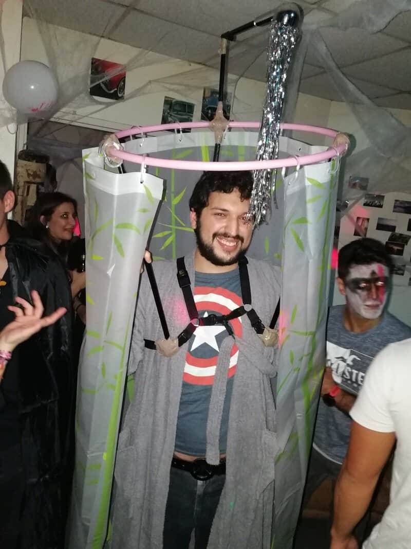 Man smiling inside a pink ring device with gray fabric, straps, and metal tubing at a Halloweenパarty.