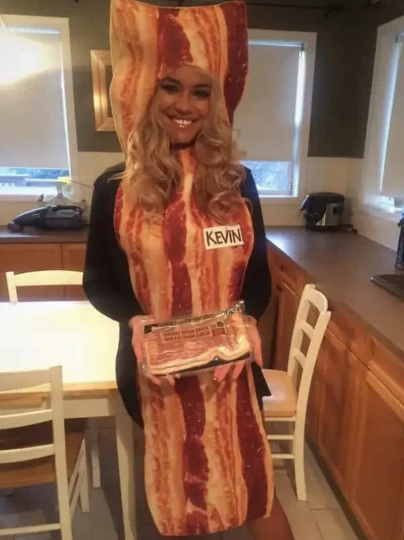 Woman wearing a bacon costume with name tag Kevin in a kitchen setting.