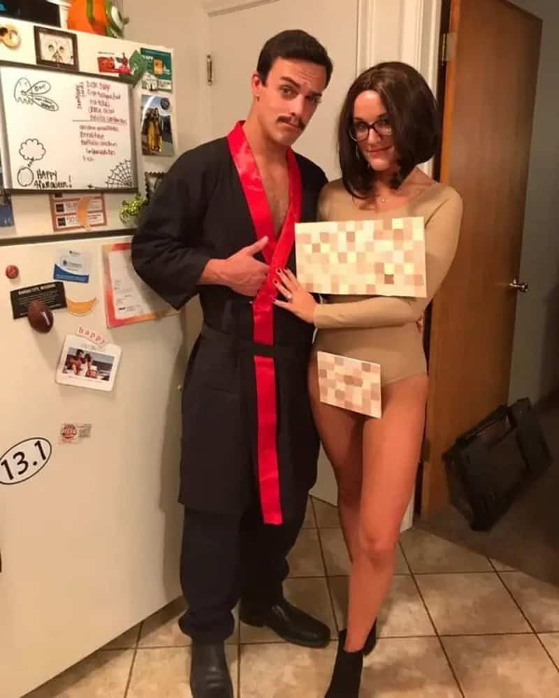 Two adults in a kitchen posing for a photo; man in black robe with red sash, woman in nude bodysuit,.