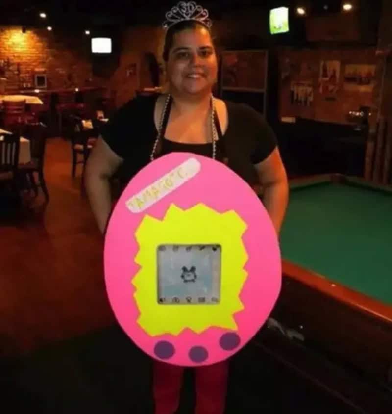 Woman wearing a tiara, black shirt, and beaded necklace posing with a large pink Easter egg cutout,.