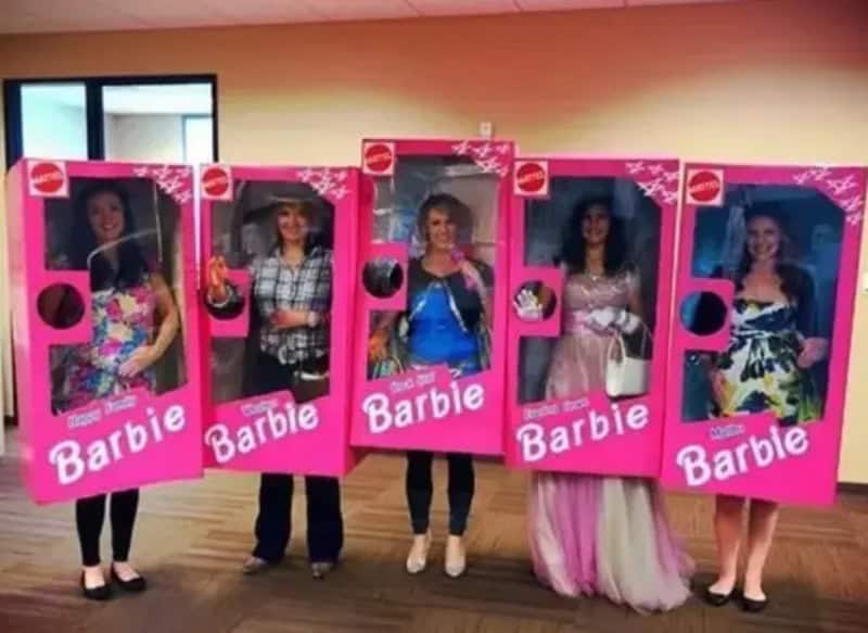Five people dressed as Barbie in pink boxed costumes line up indoors.