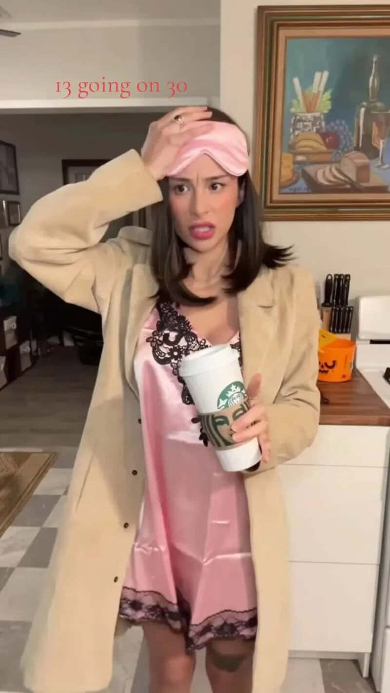Woman wearing pink headband and nightgown inside home, holding a coffee cup with a beige coat over a.
