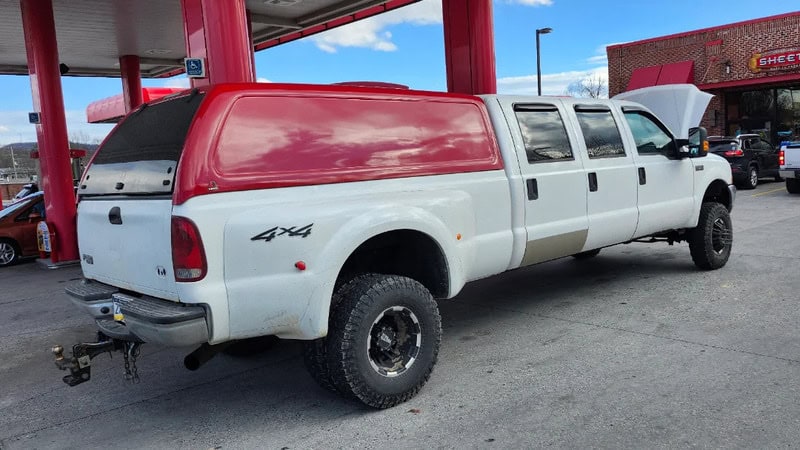 White 4x4 pickup truck with red camper shell at gas station.