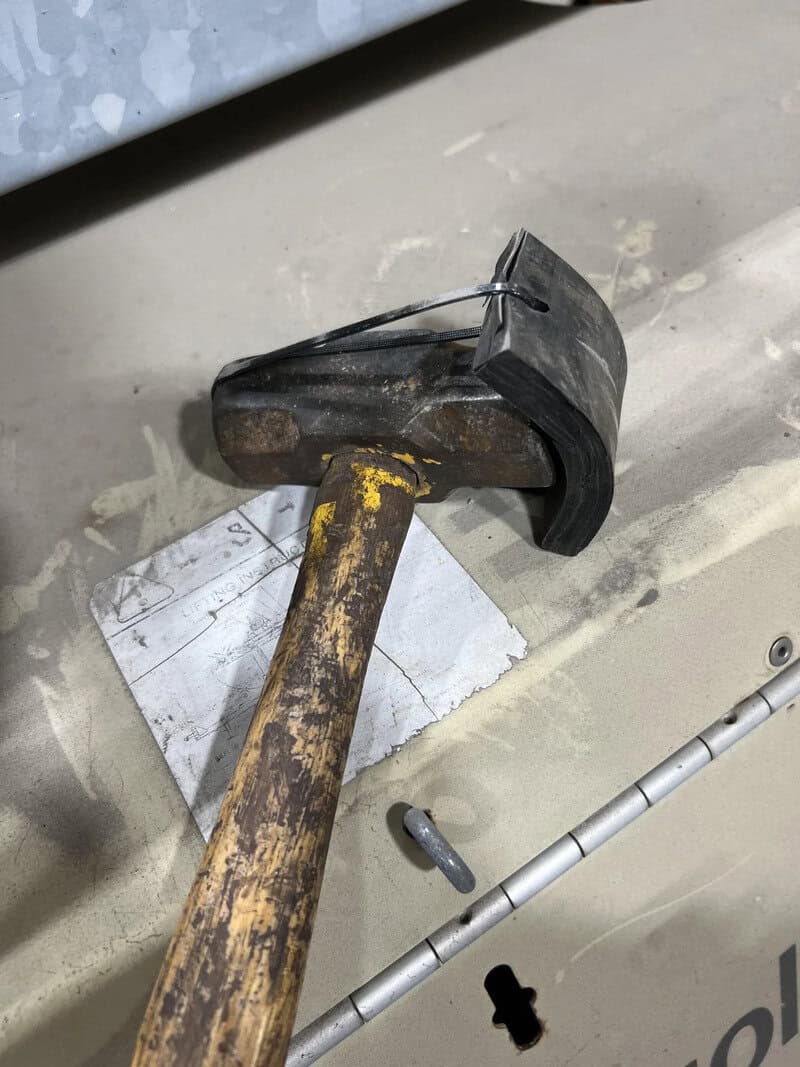 A hammer with a black head and a rusty handle on a work surface.