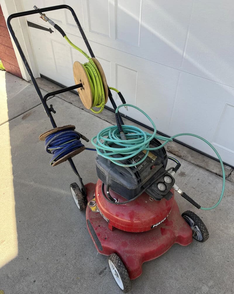 Red lawnmower with multiple extension cords and reels attached, parked on concrete.