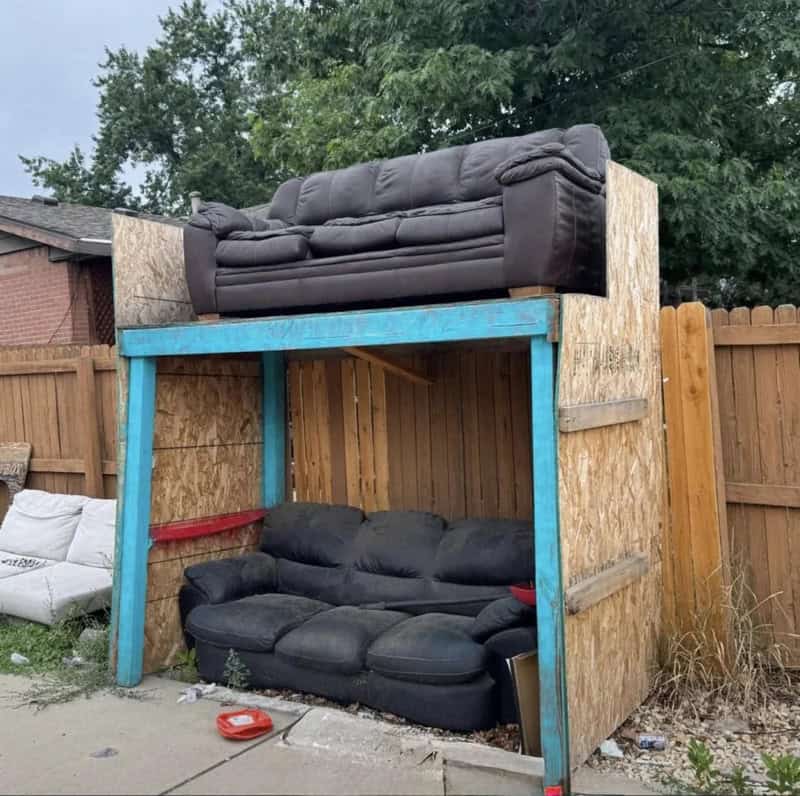 A makeshift two-level sofa structure built with wood and OSB panels in a backyard.