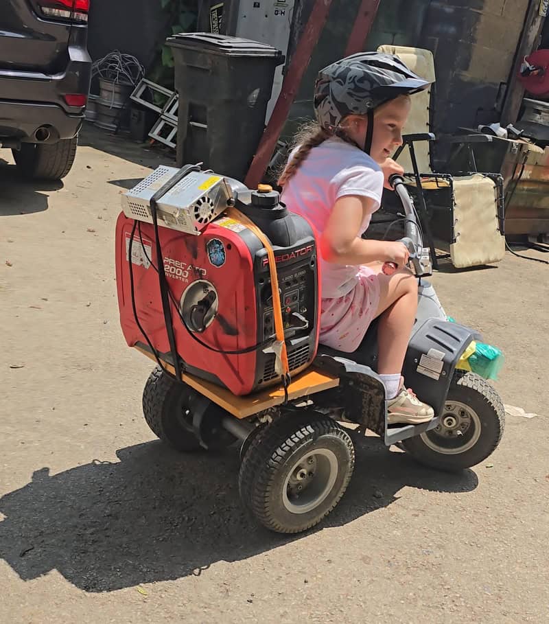 Child riding a small motorized vehicle with a generator attached, wearing a helmet.