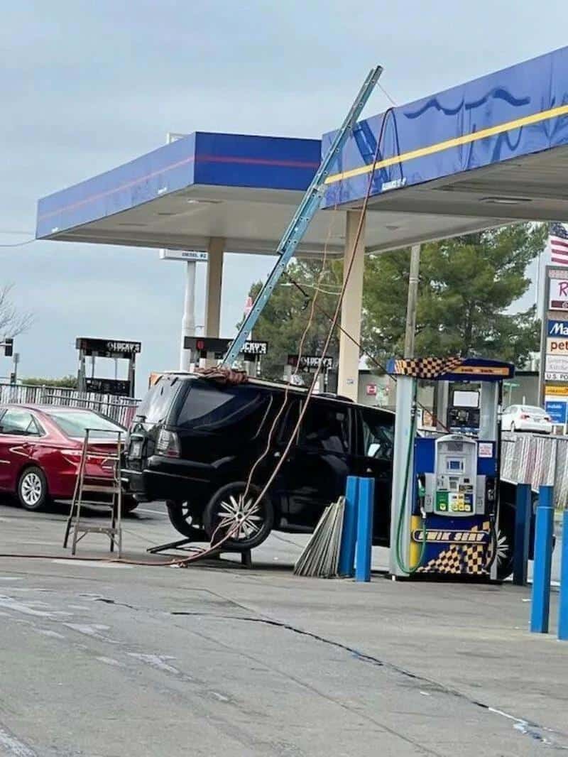 Black SUV crashed into gas pump at a convenience store, with a bent pole and damaged pump.