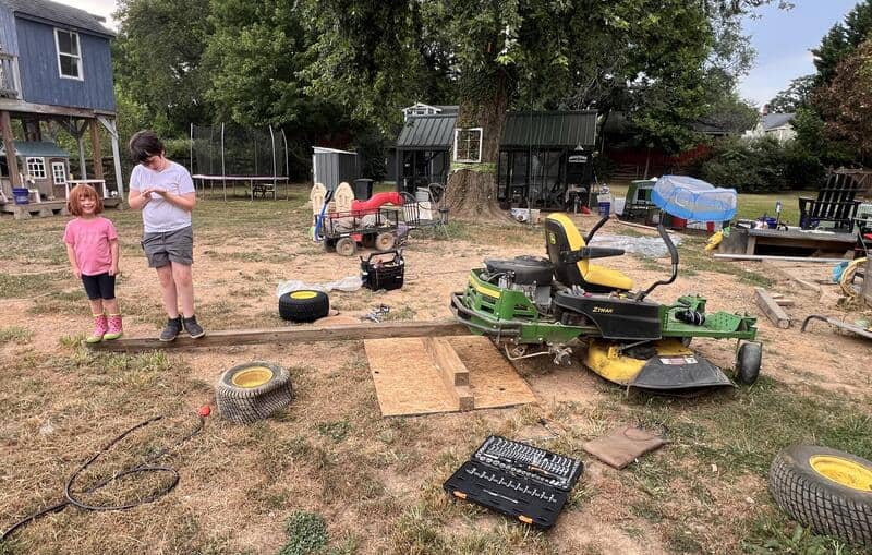 Children playing with homemade go-kart and tools in backyard.