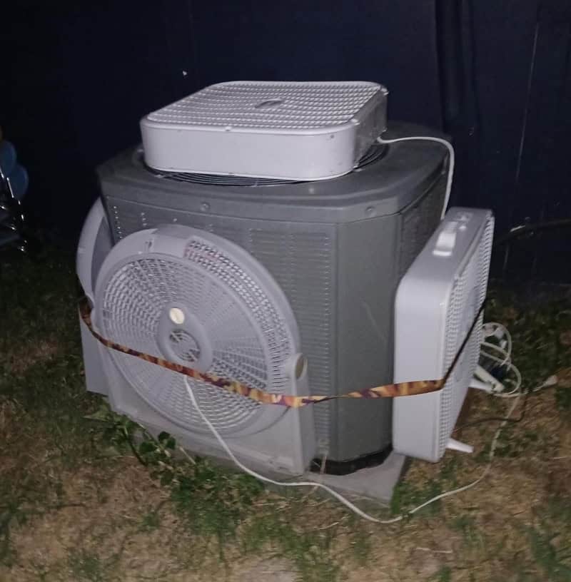 A washing machine with a fan and a small white appliance on top, secured with a strap, outdoors at n.