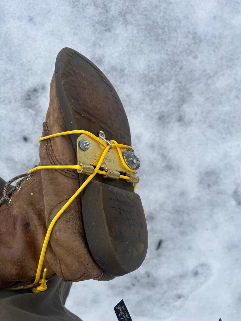 Boot with a metal spike and yellow cord on icy ground.