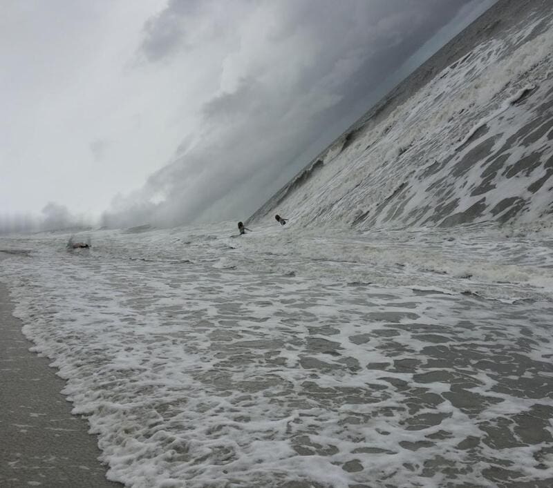 Surfers in rough ocean waves during a stormy day.