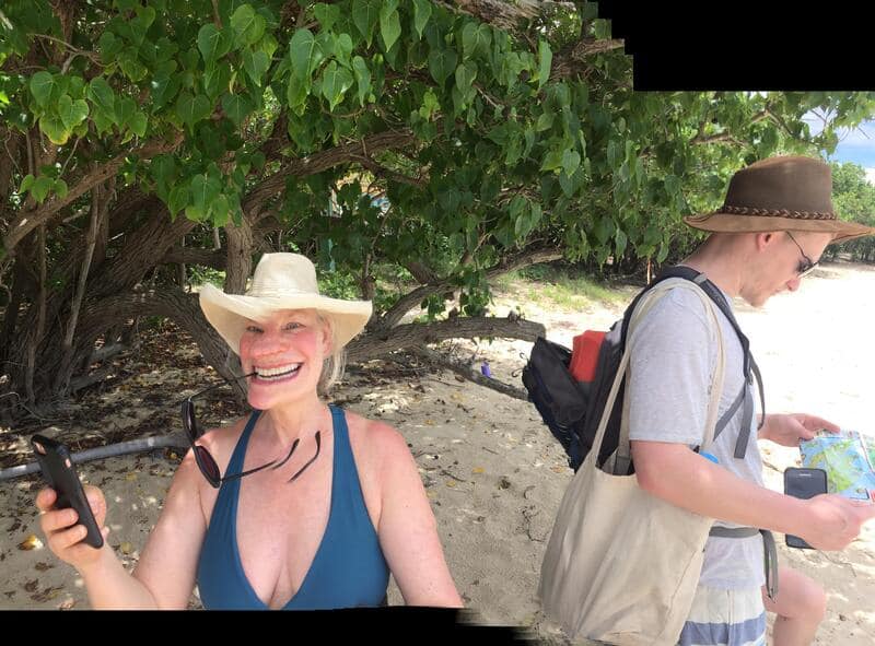 Smiling woman in a blue swimsuit and wide-brimmed hat on the beach.