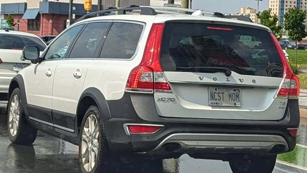 White Volvo XC70 with a humorous license plate 'NCST MOM' parked on the street.