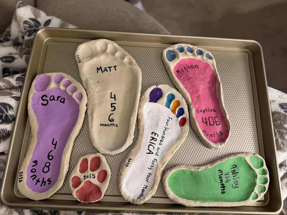 Colorful painted baby footprints with names and ages on a tray.