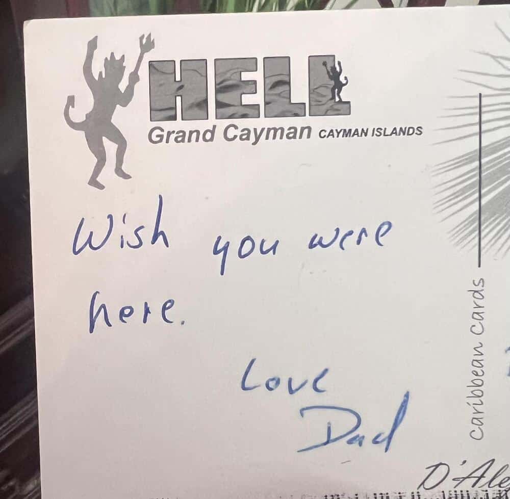 Handwritten note saying 'Wish you were here. Love Dad' on a card from Hell Grand Cayman Islands.