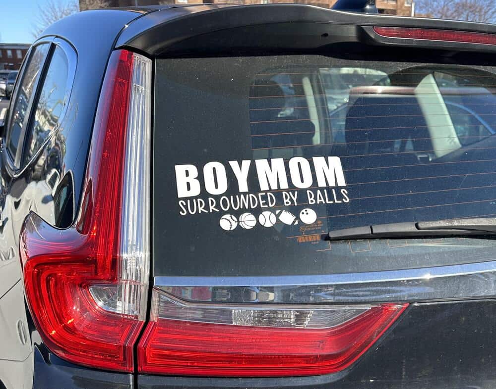 Boy mom surrounded by balls sticker on car rear window.