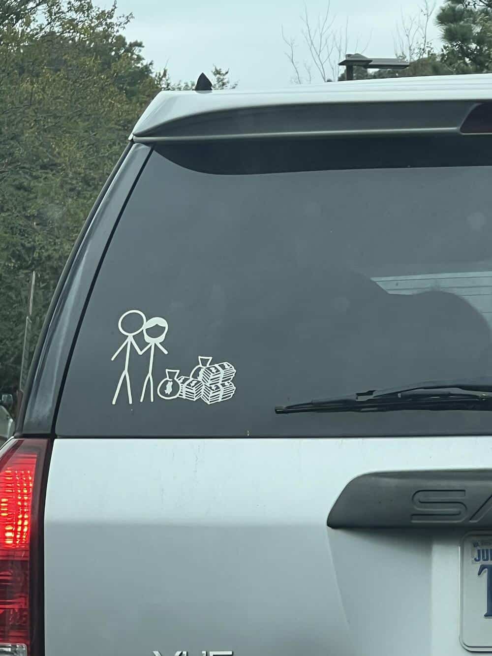 Stick figure parents with a baby and a stack of money on car window.