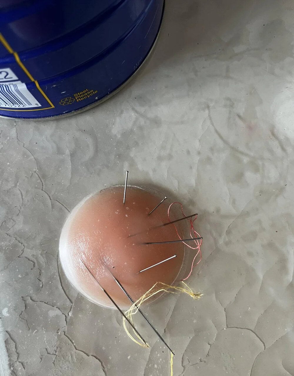 Egg with sewing pins and thread on a marble surface.