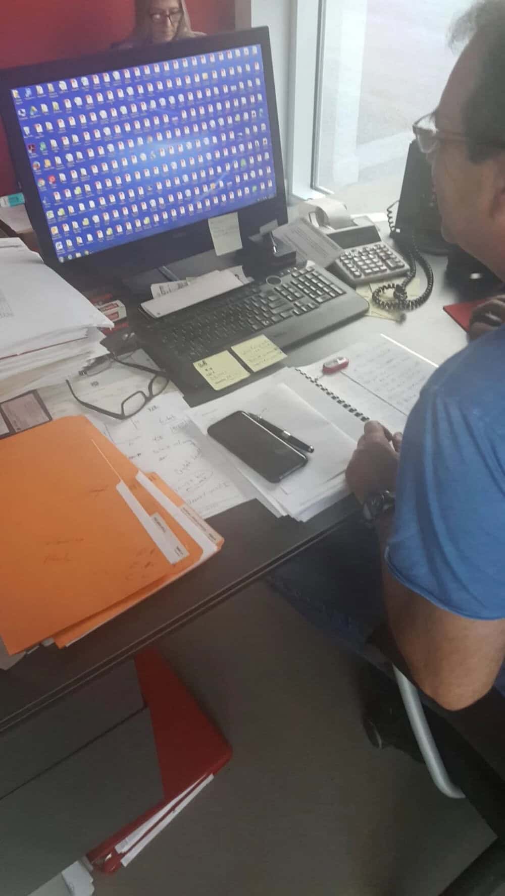 Person working at desk with computer, papers, and phone in an office.