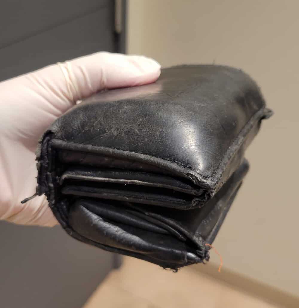 Worn, damaged black leather wallet held by a gloved hand.
