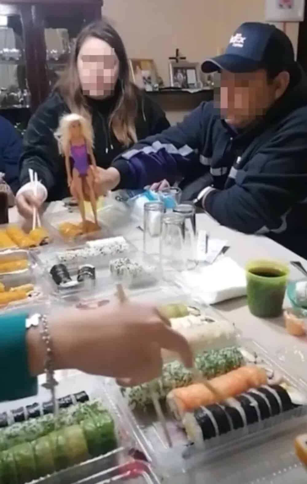 People at a table with sushi, one person holding a Barbie doll with a purple dress.