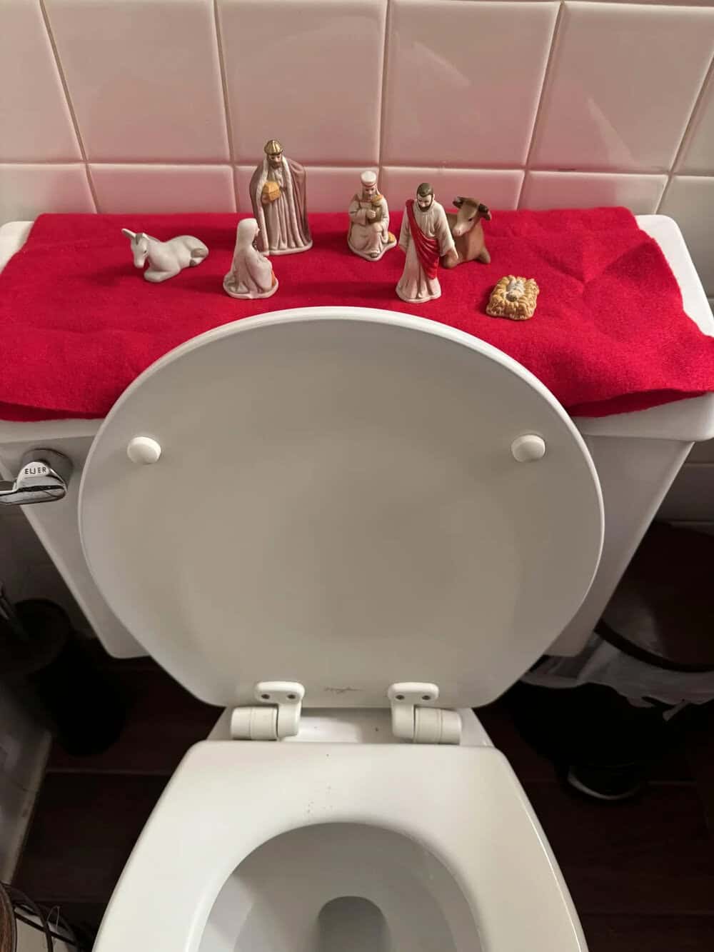 Nativity scene figurines on a red cloth on top of a toilet tank.