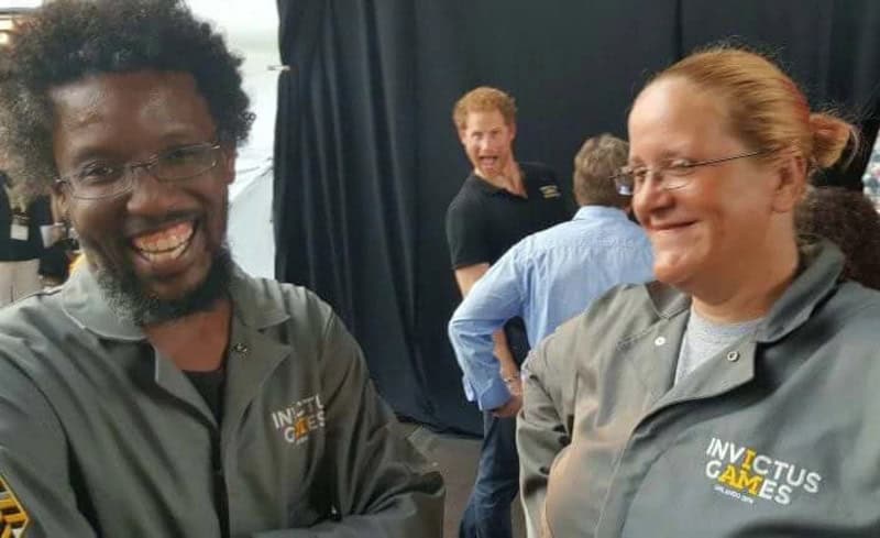 Two smiling people in gray Invictus Games jackets at a photobomb event.