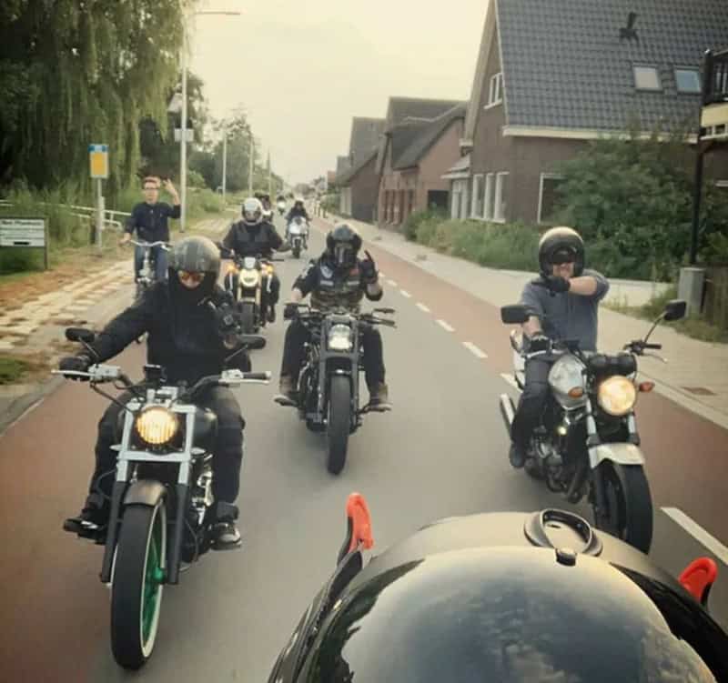 Group of motorcyclists riding on a residential street with houses and trees.
