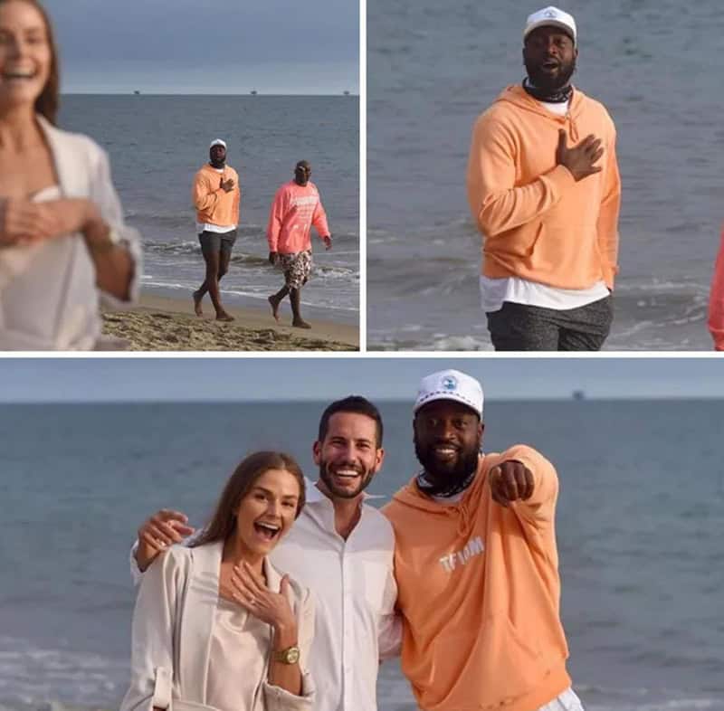 People at the beach, one man in an orange hoodie and cap, others smiling and enjoying the day.