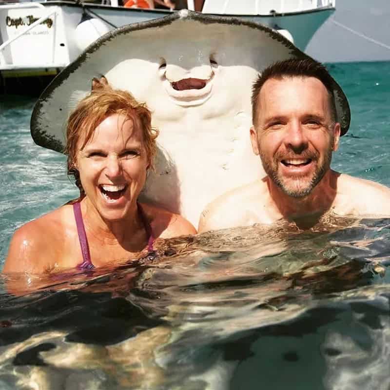 Two smiling people with a large stingray in a marina setting.