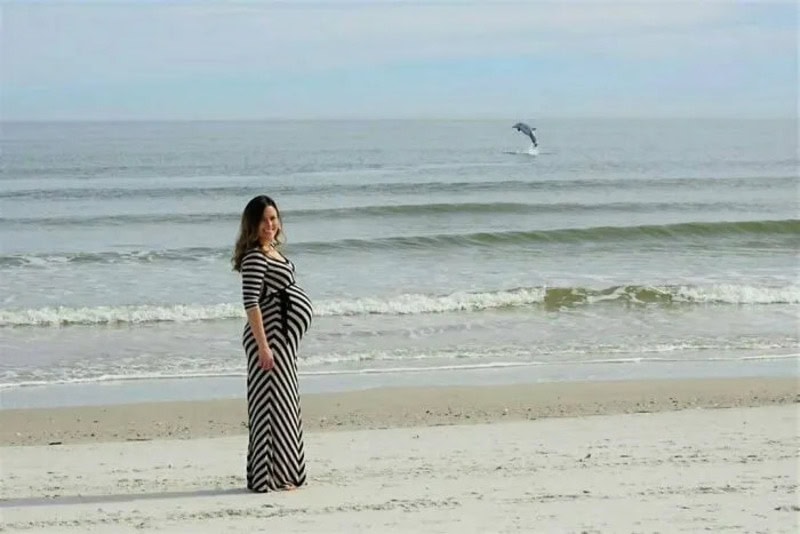 Pregnant woman in a striped dress on the beach with a seagull flying in the background.