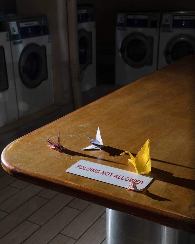 Origami paper cranes on a table with a 'FOLDING NOT ALLOWED' sign.