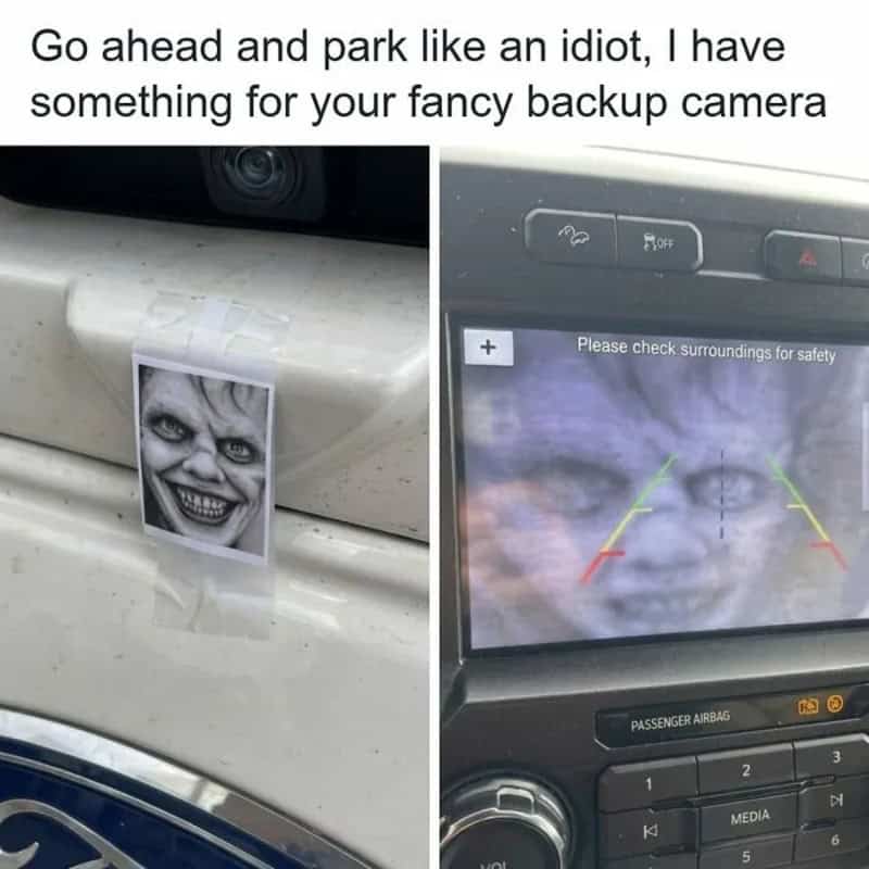 Photo of a car with a printed scary face taped to the bumper and a backup camera display showing the.