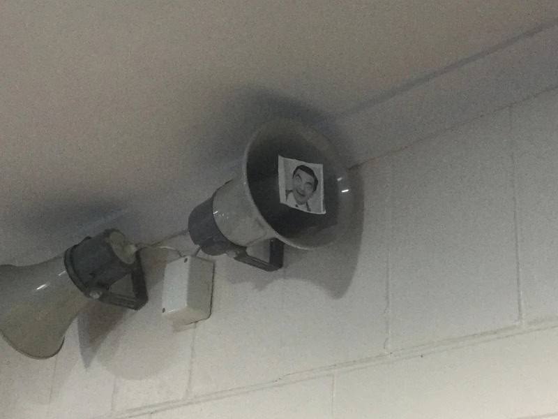 Speakers on wall with a photo of a man inside one speaker, under a megaphone.